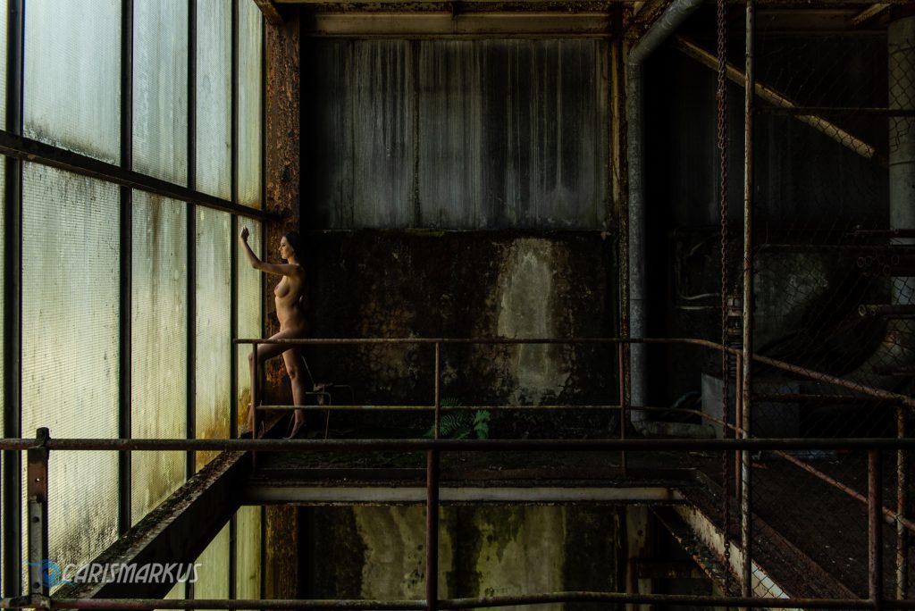 Topmodel Nikolart posing nude in an abandoned power plant in front of a colorful window between steel and rust